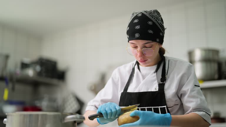 Young woman working and peeling potatoes in commercial kitchen