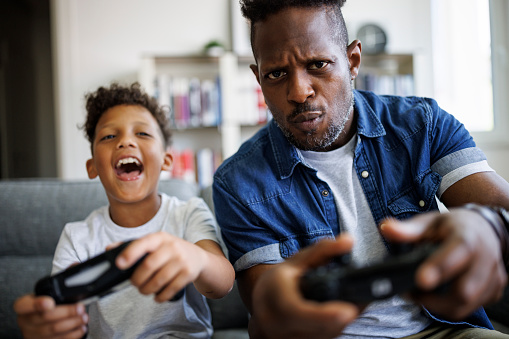 Happy African American father and his adorable mixed race son playing games in the living room at home