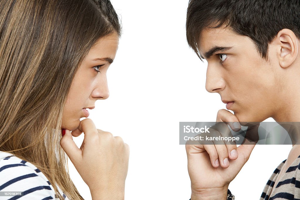 Teen coupe looking at each other wondering. Close up portrait of teen couple looking at each other with wondering expression.Isolated on white. Face To Face Stock Photo