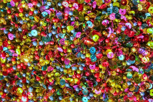 istock Close-up of colored glittering sequins texture background. Shiny festive confetti with blinking lighting. Sparkle pearlescent christmas decor. Surface shimmering abstract composition 1570190036