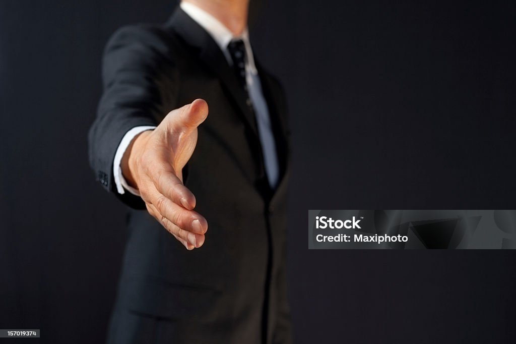 Manager handshake: business man giving hand A businessman is giving his hand for handshake, as a metaphor of successful agreement and positive business. The image has plenty of copy space and a dark background. Handshake Stock Photo