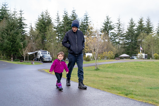 An active grandfather smiles down at his excited, two year old Eurasian granddaughter while enjoying a relaxing walk through a campground the multi-generation family is staying at while on vacation together