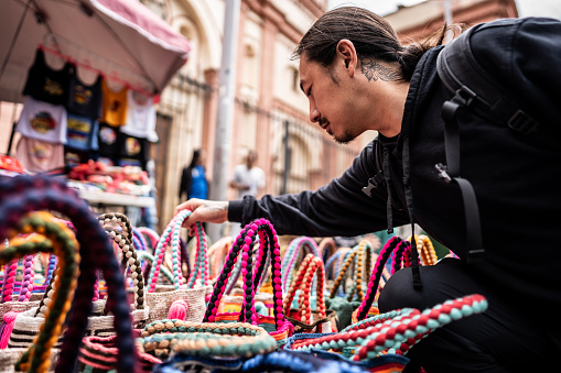Mature asian traveler looking at souvenirs bag on a street market in historic district of Bogota, Colombia