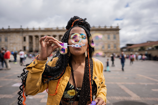 Mid adult woman playing soap bubbles in historic district in the city