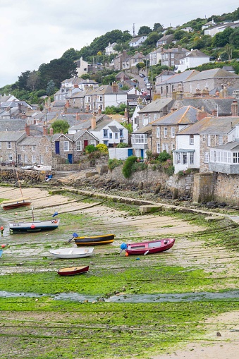 Mousehole harbour and village, with boats moored at low tide, Cornwall, England