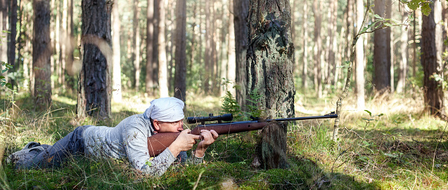 A middle-aged man shooting in the forest with his air gun. Panoramic photo.