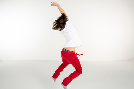 Portrait of a young boy. 10 year old boy jumping on white background. White t-shirt and red sweatpants. white people.