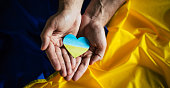 Heart in the colors of the flag of Ukraine in hands on flag background. Ending the war in Ukraine. Help and support. Strong nation. Battle for justice, freedom and democracy.