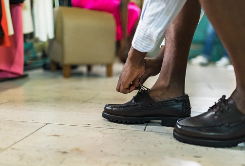 Closeup of legs, black man trying on loafer shoes at clothing store. Getting dressed for wedding.