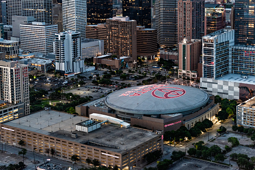 Houston, United States - April 13, 2023:  Aerial view of the Toyota Center, the home of the NBA's Houston Rockets; the sign illuminated at dusk, shot from about 600 feet in altitude from an orbiting helicopter.