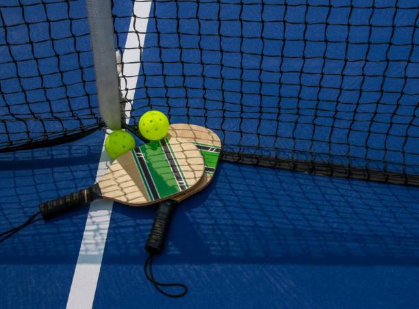 pickleball-paddel und whiffle-bälle auf einem platz am netz aus nächster nähe - racketball racket ball court stock-fotos und bilder