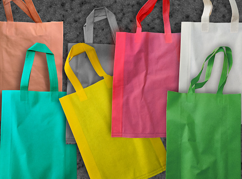 bunch of colorful polypropylene tote bags on a blurry gray background. spunbond bag