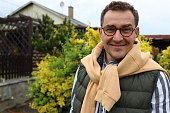 Portrait of a mature smiling businessman with glasses in yellow hoodie standing in garden and looking in camera