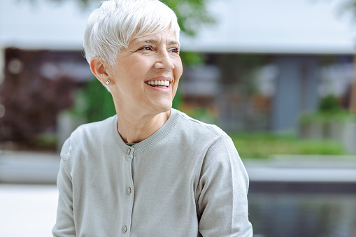 Happy senior woman with gray short hair relaxing on bench and looking away