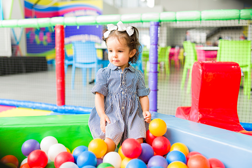 Adorable little kid playing in the ball pit of the indoor playground and having fun while enjoying her fun game