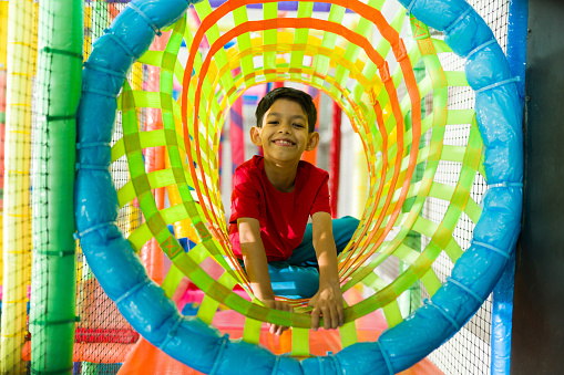 Excited hispanic little boy smiling while having a fun recreation time playing a game in the colorful playground
