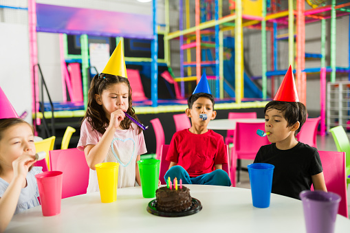 Group of happy children ready to eat cake during a birthday party with friends having fun in the indoor playground