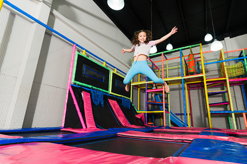 Cheerful young child looking excited laughing while jumping in the air and having fun on the indoor trampoline