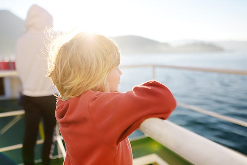 Blond little child is traveling with family by ferry. Schoolboy is enjoying the landscape of the Adriatic Sea. Cruise ship vacation during the holidays.