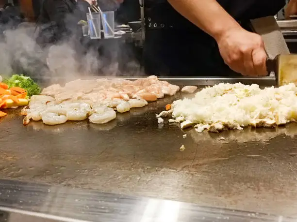 Chef cooking fried rice, shrimp and vegetables at a hibachi teppanyaki restaurant