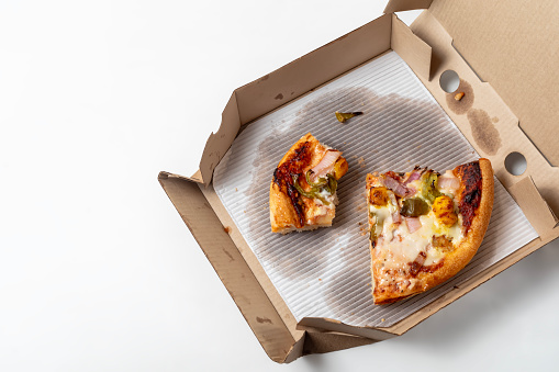 Leftover pizza in an open cardboard pizza box isolated on white background.