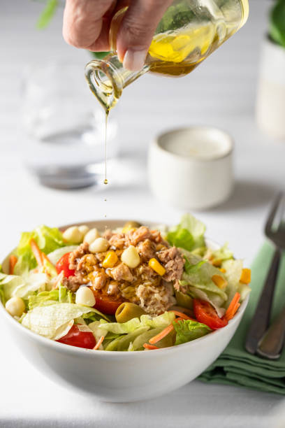 istock Hand adding a dressing into the tuna salad with lettuce and vegetables on the table 1570673730