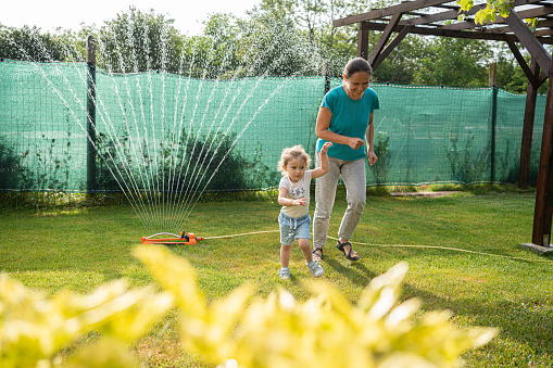 Mother and her cute little children playing with water with garden hose in a backyard