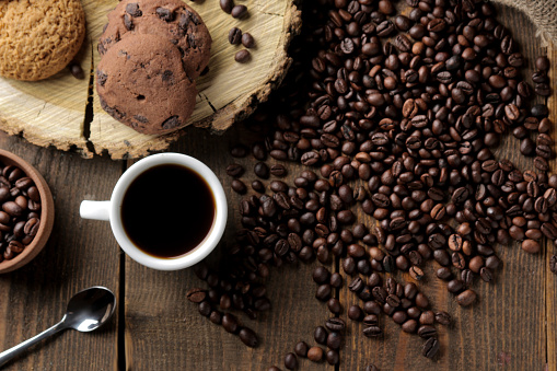 Roasted coffee grains and a cup of coffee and cookies on a brown wooden background. Robusta, Arabica. top view