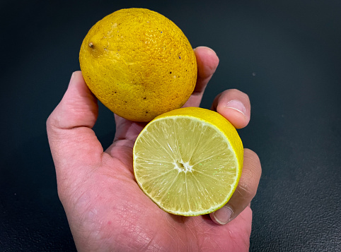 Hand with fresh lemon fruit on black background
