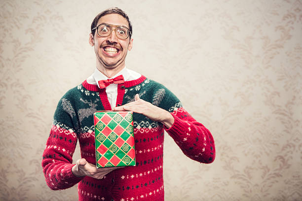 Christmas Sweater Nerd A man in a knit reindeer Christmas cardigan button up sweater, complete with matching red bow tie and a classy mustache shows off a wrapped gift he's ready to give as a present.  Damask style vintage wall paper in the background.  Horizontal with copy space. christmas nerd sweater cardigan stock pictures, royalty-free photos & images