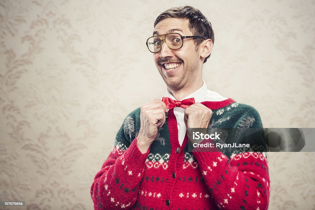 Christmas Sweater Nerd A man in a knit reindeer Christmas cardigan button up sweater, complete with matching red bow tie and a classy mustache.  He straightens his bow tie with a cheesy smile on his face, proud of his fashion style.  Damask style vintage wall paper in the background.  Horizontal with copy space. Christmas Stock Photo