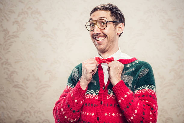 Christmas Sweater Nerd A man in a knit reindeer Christmas cardigan button up sweater, complete with matching red bow tie and a classy mustache.  He straightens his bow tie with a cheesy smile on his face, proud of his fashion style.  Damask style vintage wall paper in the background.  Horizontal with copy space. facial hair photos stock pictures, royalty-free photos & images