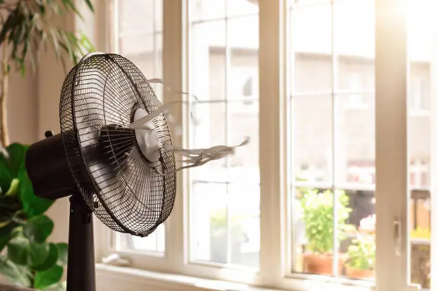 Electric cooling fan with blowing ribbons in front of window on hot summer day