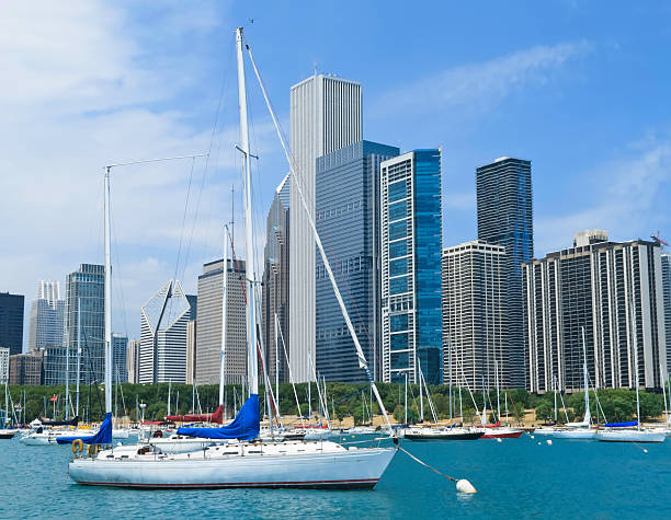 Urban view of the Chicago River surrounded by modern skyscrapers, residential buildings, and trees, with boats docked along the river on a partly cloudy day.