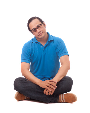 Attractive young Asian student  sitting on the floor, isolated on white, smiling and pointing to camera