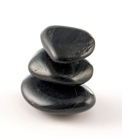 Rounded black volcanic pebble stones on top of each other on white background