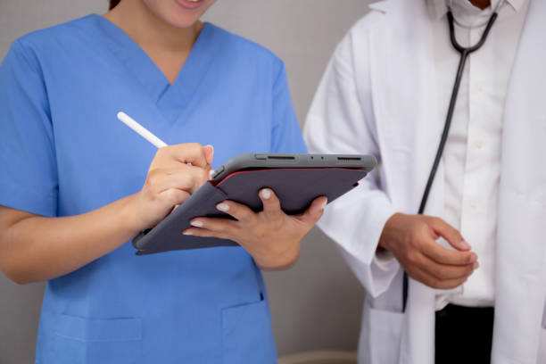 Closeup hands nurse writing report medical and health care on tablet while specialist doctor explaining and check and diagnostic with elderly patient in hospital, examining disease, senior and unwell. stock photo