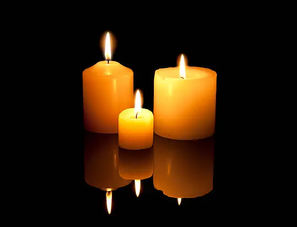 Three burning candles with reflexion on a black background