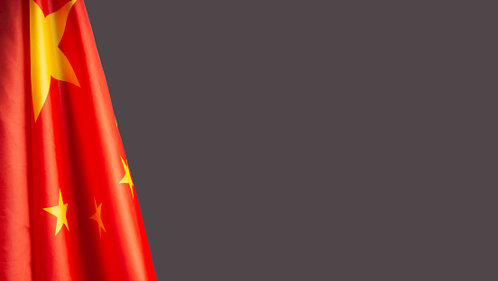 A Close-up of the Chinese flag is on the left side on a gray background with copy space for text