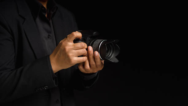 istock Close-up of hand holding the digital camera while standing on a black background 1571005627