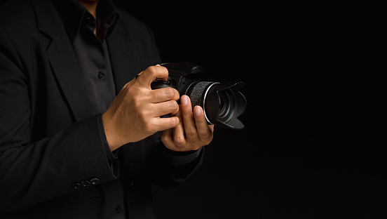 Photographer with a camera. Close-up of hand holding the digital camera while standing on a black background. Space for text