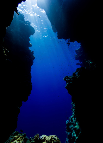 Sun beams filtering down from the surface through blue water at the exit from a shallow water sea cavern in the northern Red Sea