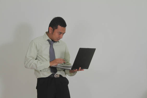 Side view of mature Asian man smiling happily holding laptop