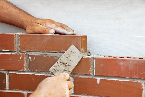 Bricklayer hands with trowel building brick wall