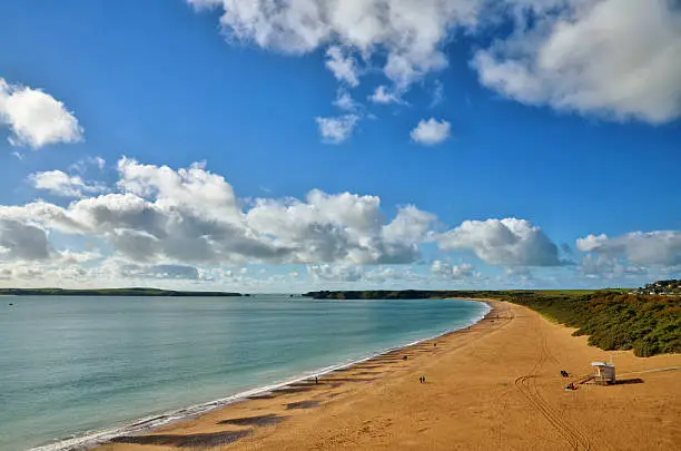 Panoramic view of South Beach, Tenby, curving towards Giltar Point and Caldey Island, with a blue sky and cumulus clouds.