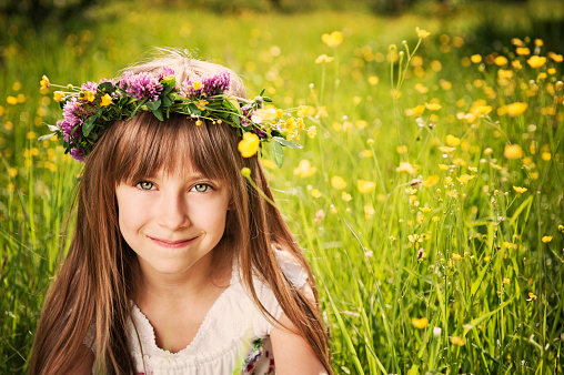 Cute little girl wearing wreath in grass and flowers.