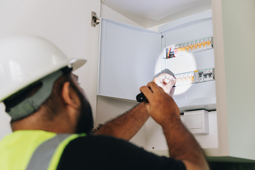 Electrician checking on the electric circuit board with torchlight