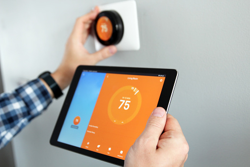 Man is Adjusting a  temperature using a tablet with smart home app in modern living room