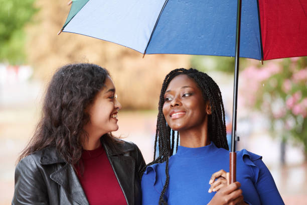 istock Multi-ethnic female friends smiling while walking outdoors with a colorful umbrella. 1571222499