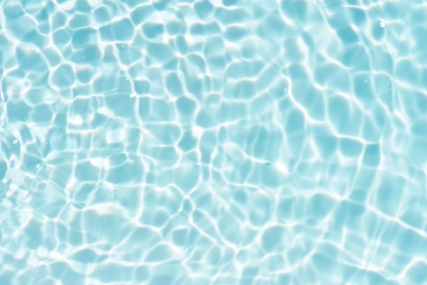 istock Blue water with ripples on the surface. Defocus blurred transparent blue colored clear calm water surface texture with splashes and bubbles. Water waves with shining pattern texture background. 1571246378